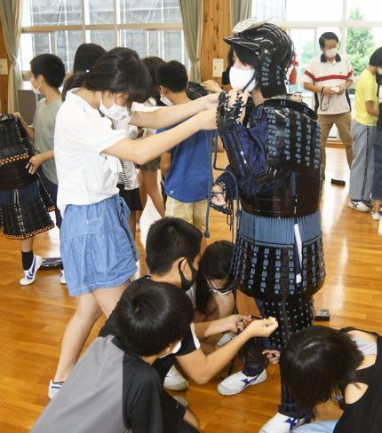 力を合わせて鎧兜のレプリカを装着する児童ら（南国市の久礼田小学校）