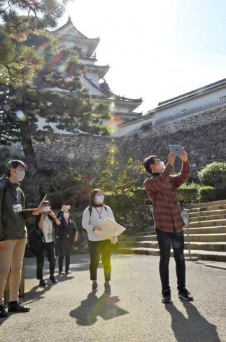 タブレット端末を手に高知城を観光する、身代わり役の柴田恵介さん＝右（高知市の高知城）