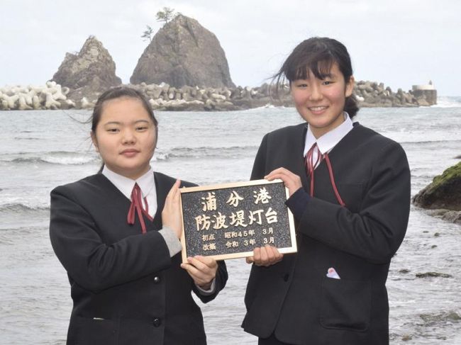 灯台が建つ予定の防波堤をバックに、銘板を手にする興津中学校の生徒（四万十町興津）