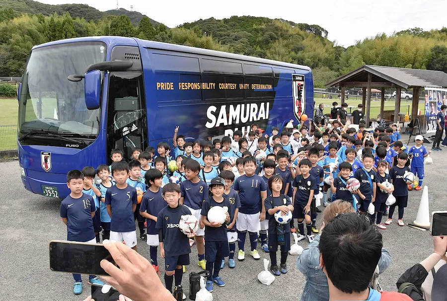 サッカー日本代表のバスと記念撮影する子どもたち（高知市の県立春野総合運動公園）