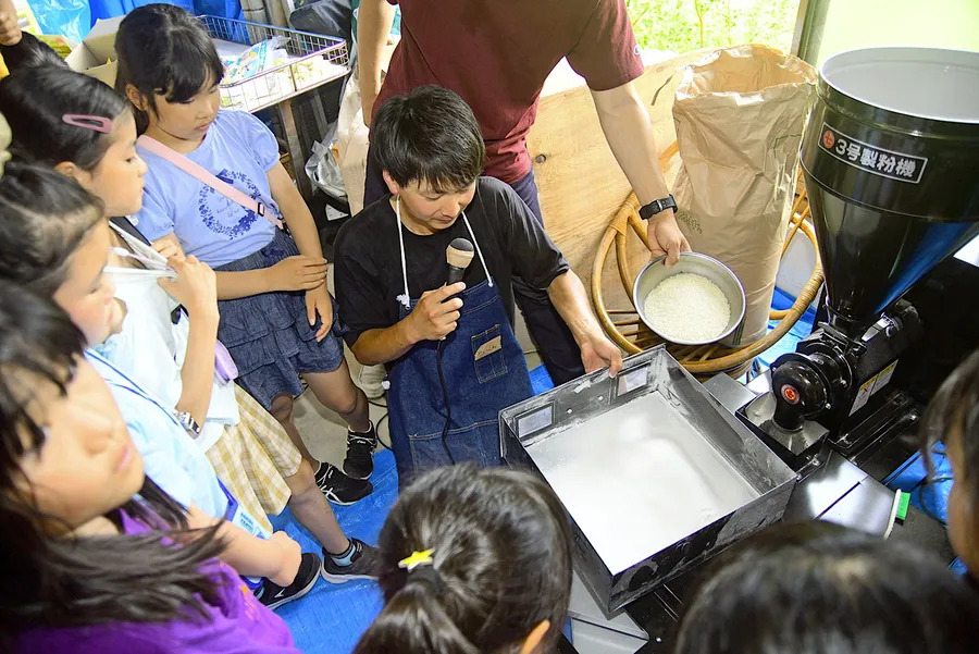 製粉機にかけられ、パウダー状になった米粉を見学する子どもたち（土佐清水市下ノ加江）