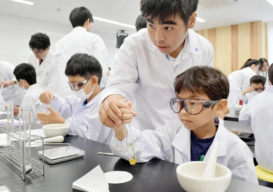 明徳義塾中高の生徒の手助けでミカンの皮を使った実験を行う児童たち（高知市の牧野植物園）
